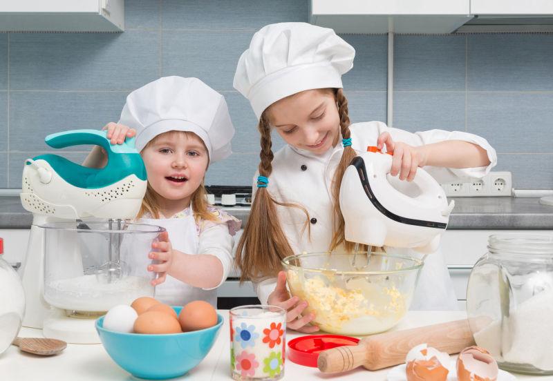 厨房餐桌上的配料和穿着厨师制服的两个孩子