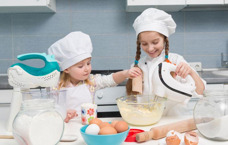 在餐桌上摆配料的穿着厨师制服两个孩子