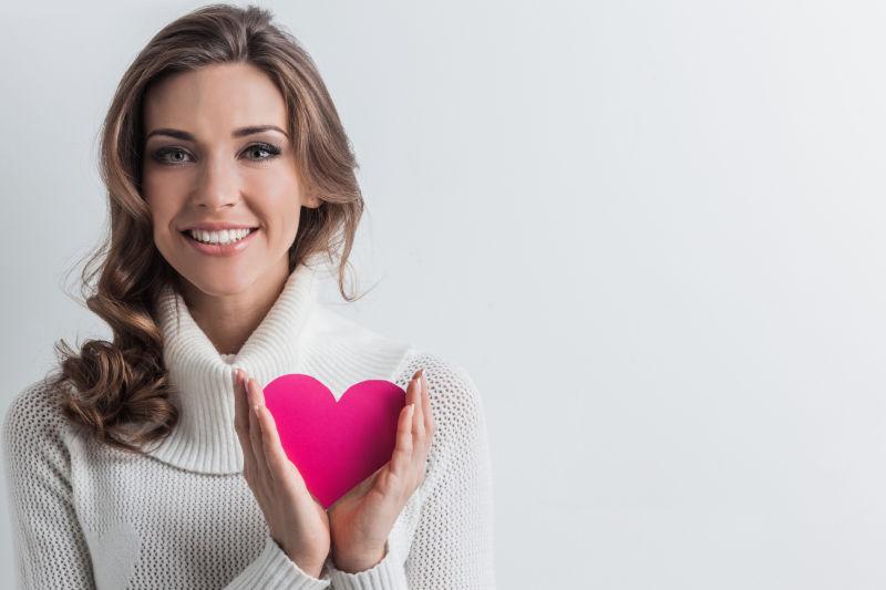 微笑的年轻女人拿着粉红纸心