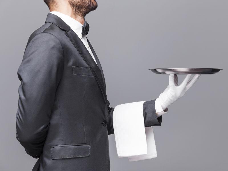 灰色背景下抱银托盘的侍者
