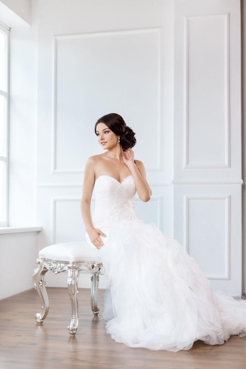 穿着漂亮衣服的新娘坐在室内的白色椅子上