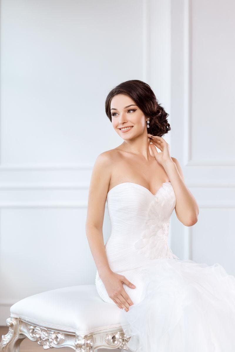 穿着漂亮的衣服坐在室内的白色椅子上的轻迷人的新娘