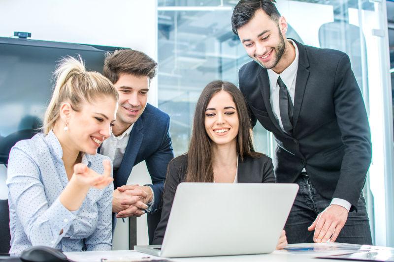 一群年轻微笑的商人在看笔记本电脑