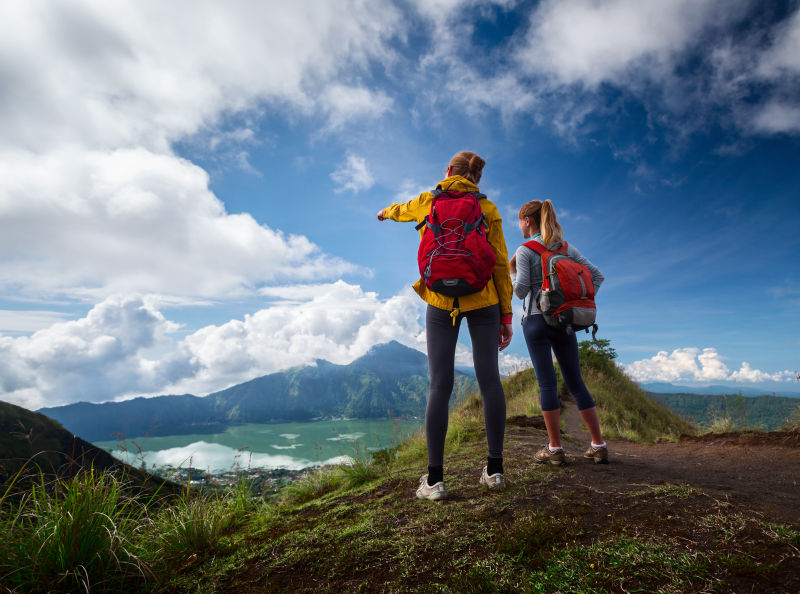 站在山顶上欣赏风景的两个背着背包的女士