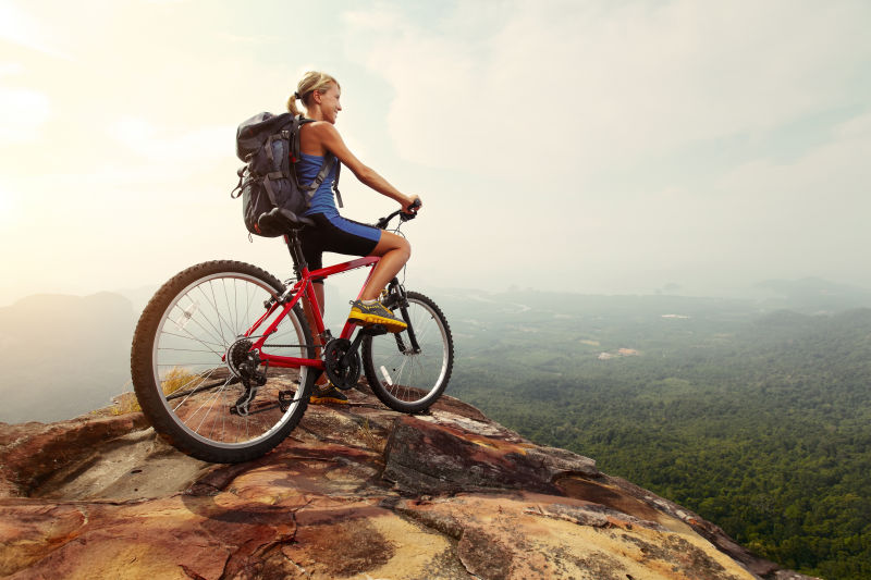 骑着红色自行车在山顶上欣赏山谷风景的年轻女子