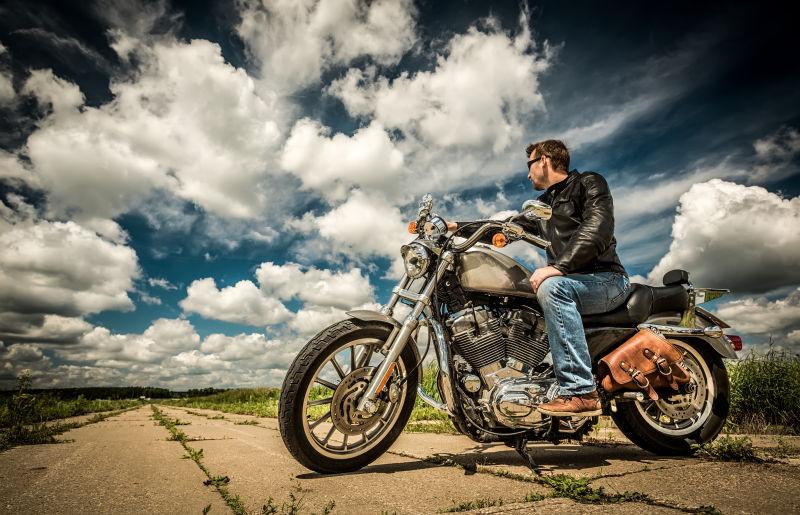 蓝天背景下戴太阳镜穿皮夹克 骑摩托车的男人
