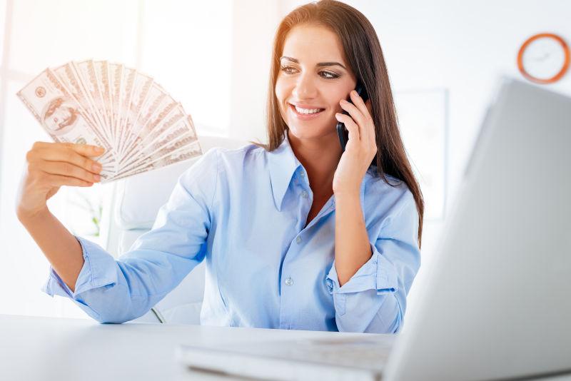 成功的女商人在办公室里拿着钱打电话