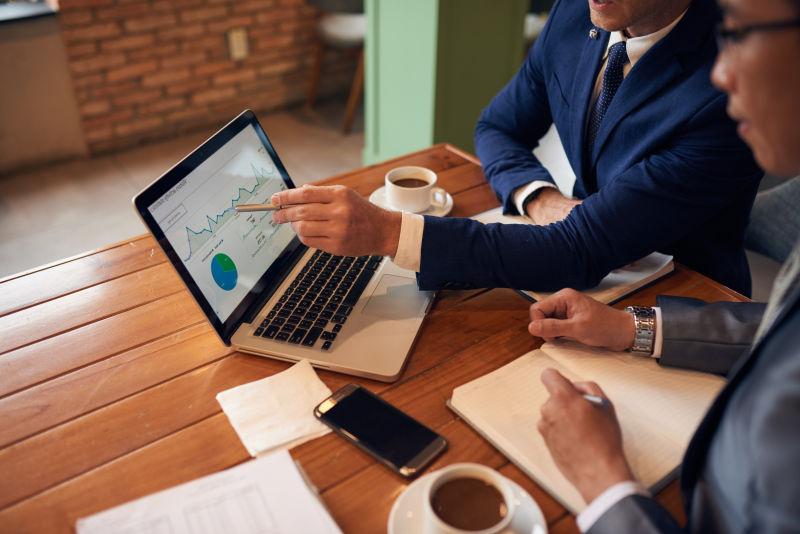 商人在笔记本电脑屏幕上向同事解释图表