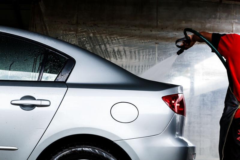 手拿喷水枪给白色汽车洗车