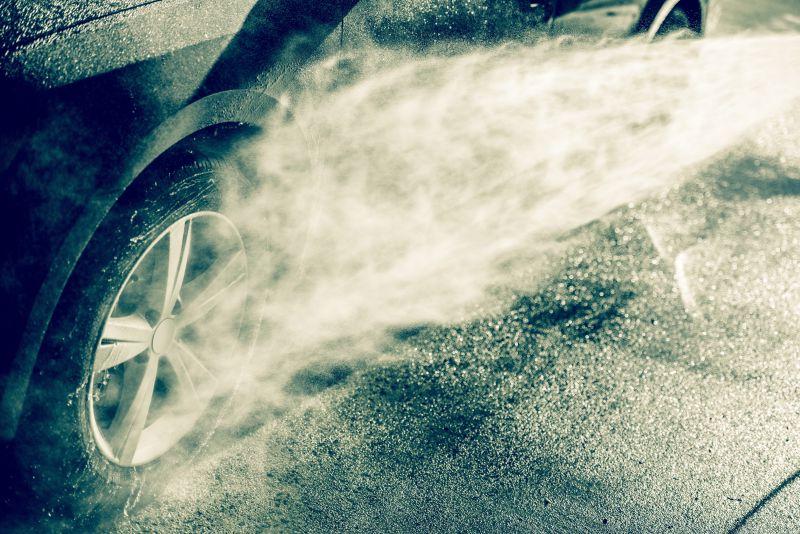 手拿喷水枪给黑色汽车车轮清洗