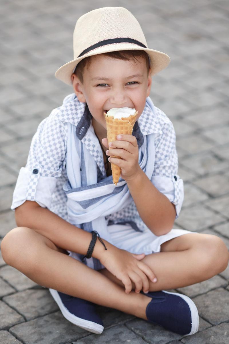 盘坐在地上吃冰淇淋戴草帽的小孩