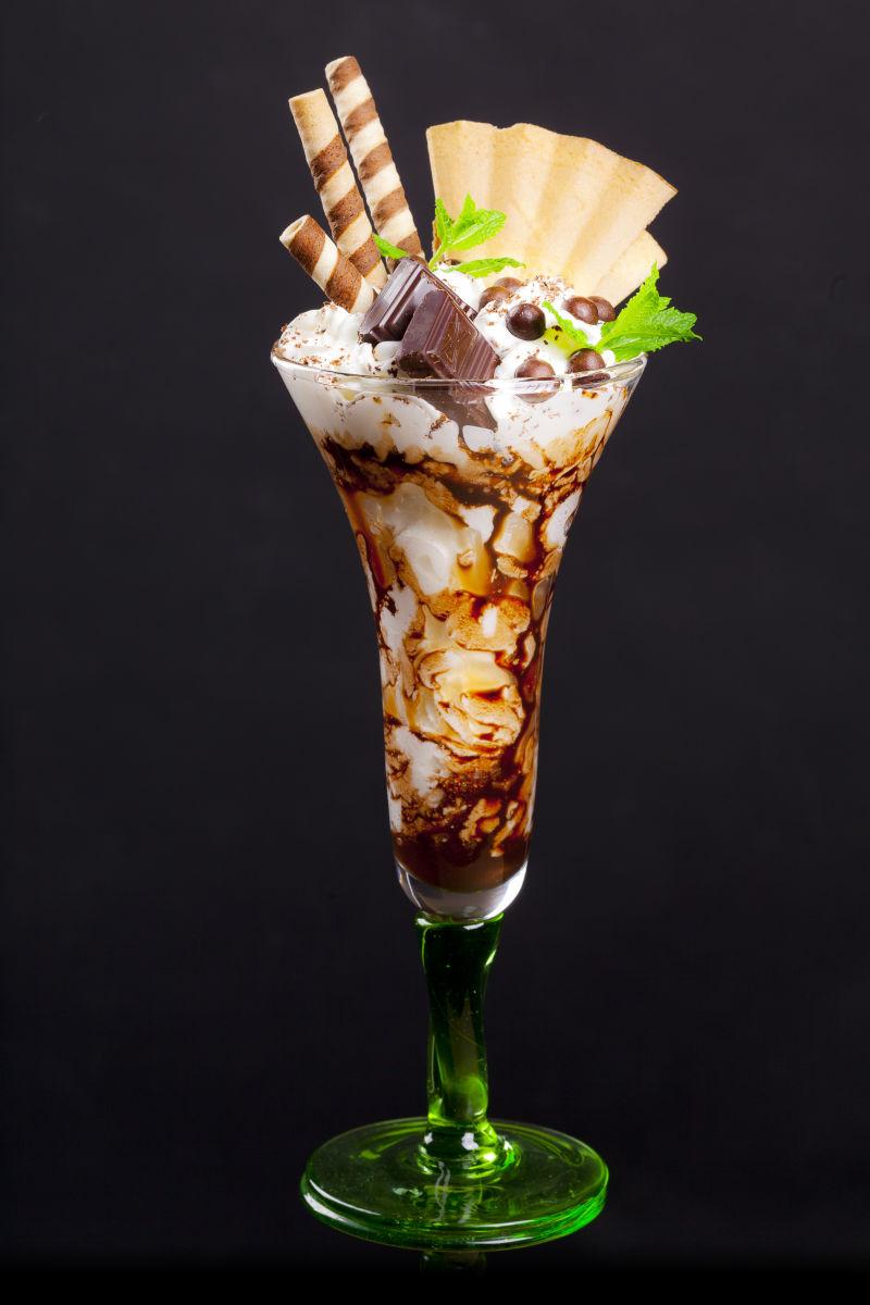 黑色背景上的淡绿色鸡尾酒杯里带有巧克力的奶油和水果