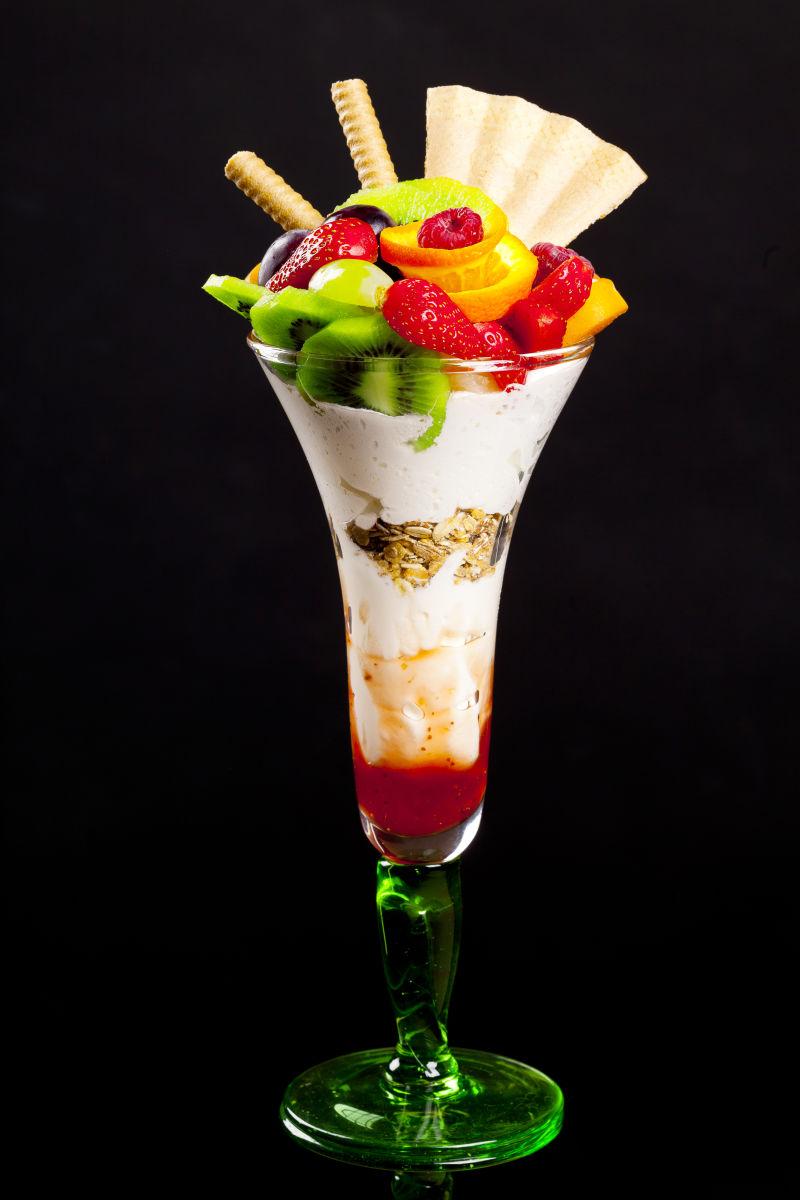 黑色背景下淡绿色鸡尾酒杯里的奶油和水果