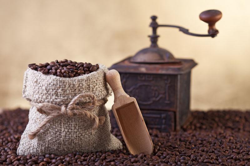 黄色背景下咖啡豆上的老旧咖啡豆研磨机和一亚麻袋咖啡豆