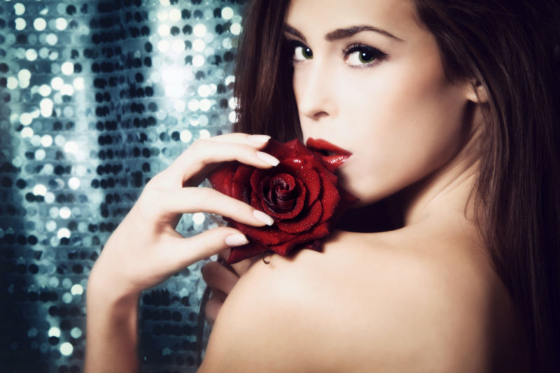 闪亮背景上拿着红玫瑰的年轻美女