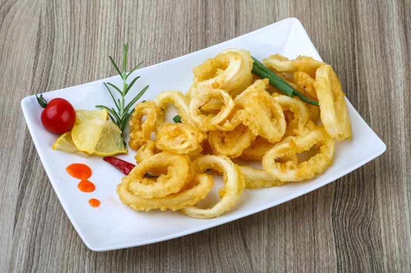 木桌上放在白色餐盘俩的黄色油炸鱿鱼圈