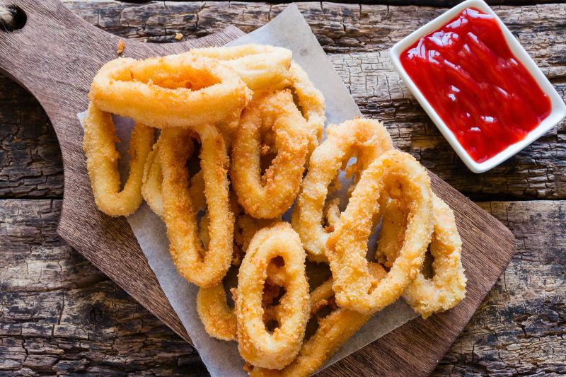 放在砧板包装纸上的炸鱿鱼圈和红色的番茄酱