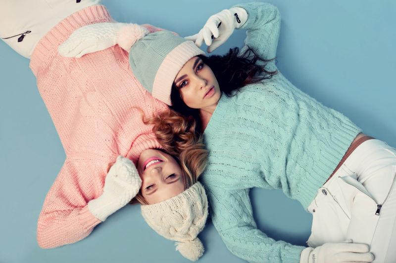 蓝色地板上的躺着两个带着针织帽的美女