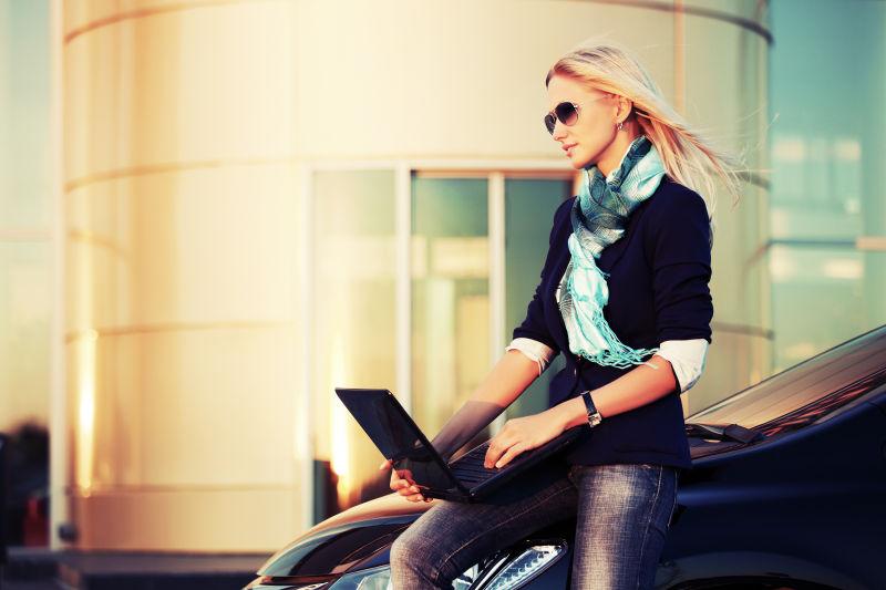 年轻时尚女商人用笔记本电脑在停车场停车