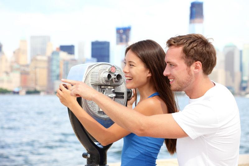 埃利斯岛的曼哈顿和纽约的天际线背景下的玩望远镜的情侣