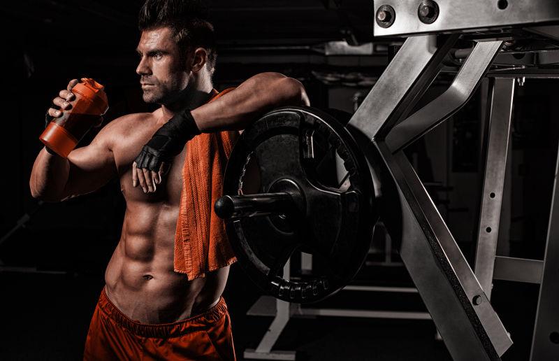 靠在健身器材旁边喝水的健身男子