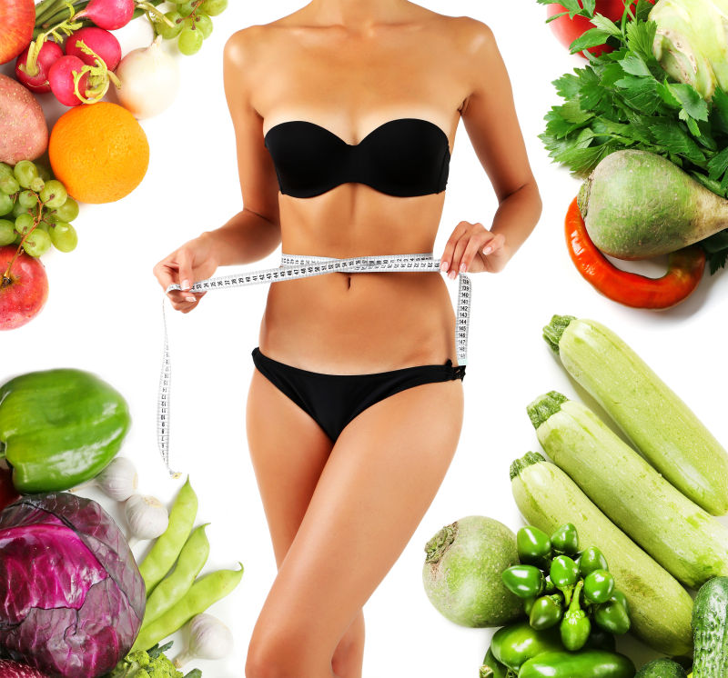 美丽的年轻女子用白色和蔬菜周围的胶带测量她的身体