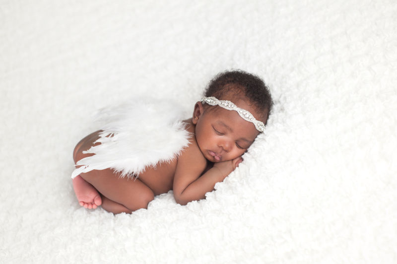 戴着羽毛翅膀趴在白色地毯上睡觉的非洲婴儿