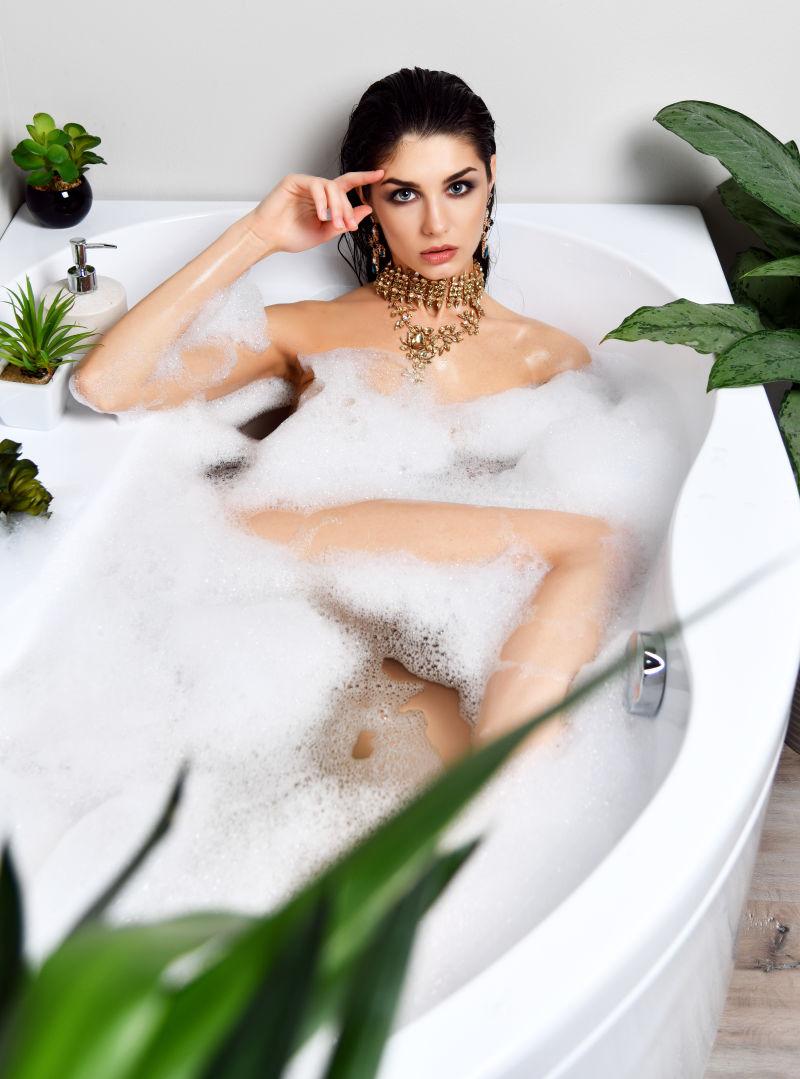 白色背景上戴着首饰躺在浴缸泡沫里的性感美女