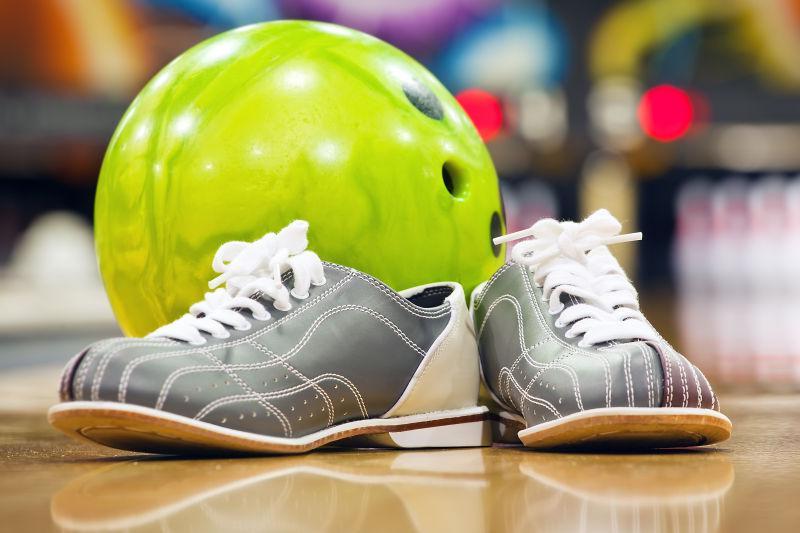 黄色木地板上的绿色的保龄球和灰色的运动鞋