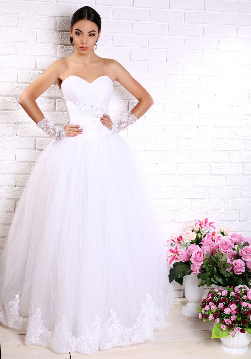 穿着优雅的婚纱的黑色的头发的美丽的新娘摆在鲜花之间