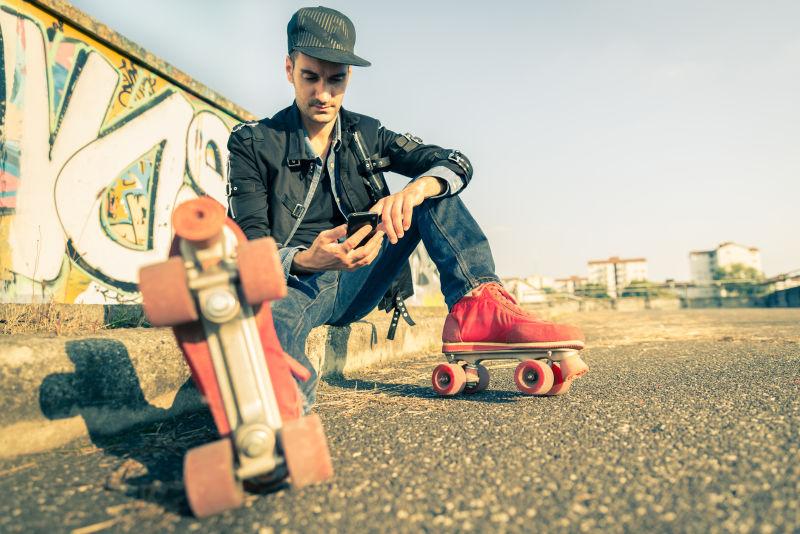 穿着溜冰鞋坐在路边玩手机的男人