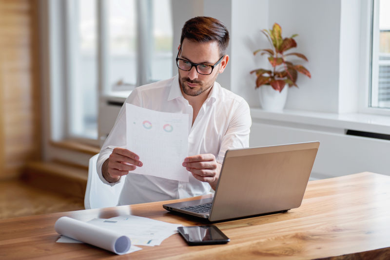 笔记本电脑前商人看着手里的文档