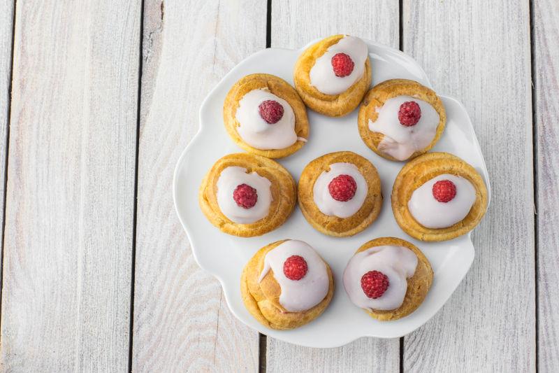 木桌上白色盘子里的白巧克力和树莓点缀的蛋糕甜点