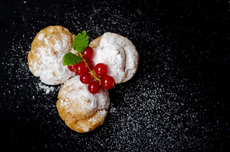 黑色背景上撒了糖霜用红色浆果装饰的蛋糕甜点