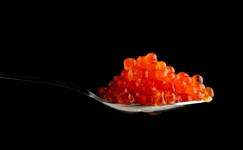 黑色背景中的金属勺子中的红鱼子酱