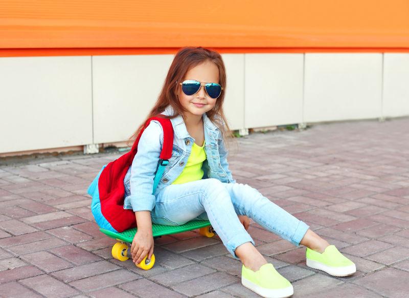 城市街头坐在滑板上的时尚小女孩