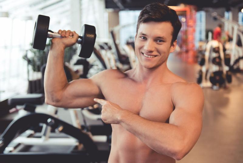 有魅力的年轻肌肉发达的男人拿着哑铃微笑着