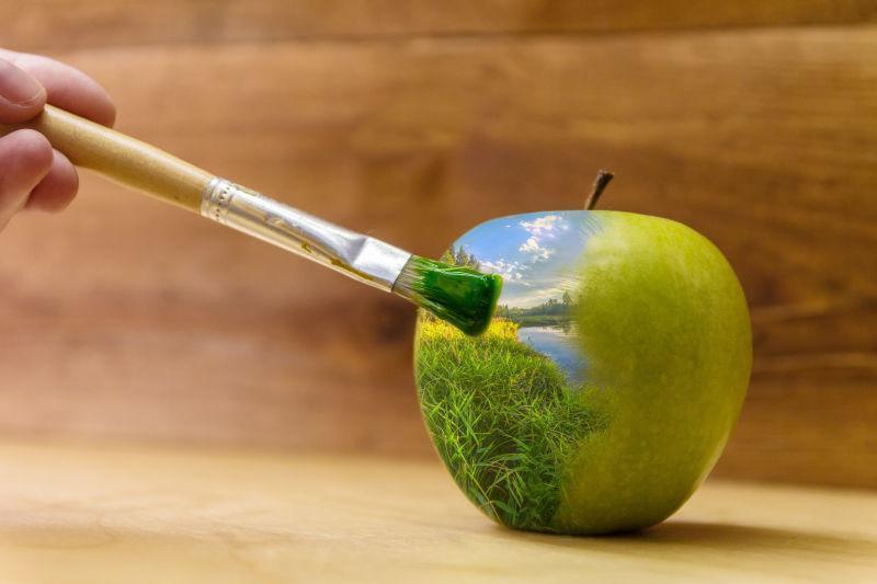 用画笔在苹果上画蓝天下的绿色植物