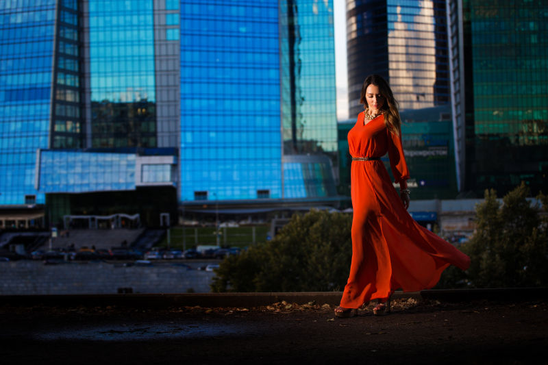 摩天大楼背景上穿着红色长裙的美女