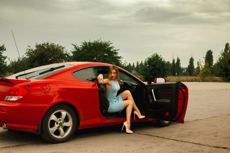 穿高跟鞋的性感年轻女子坐在一辆红色跑车上眺望阴天