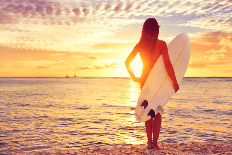 夕阳下拿着冲浪板的美女