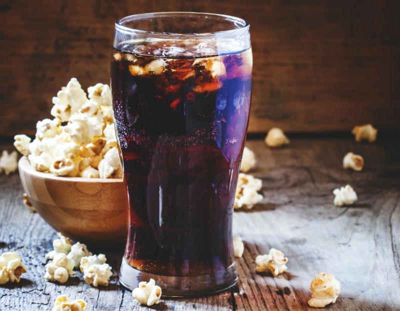 冷可乐在玻璃和大甜爆米花在碗上的旧木本背景