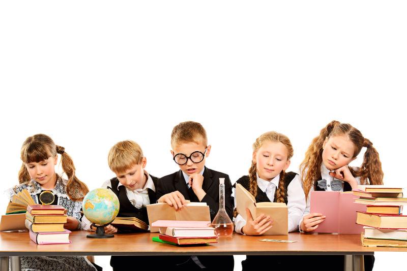 白色背景下坐在木桌前看书的五个孩子