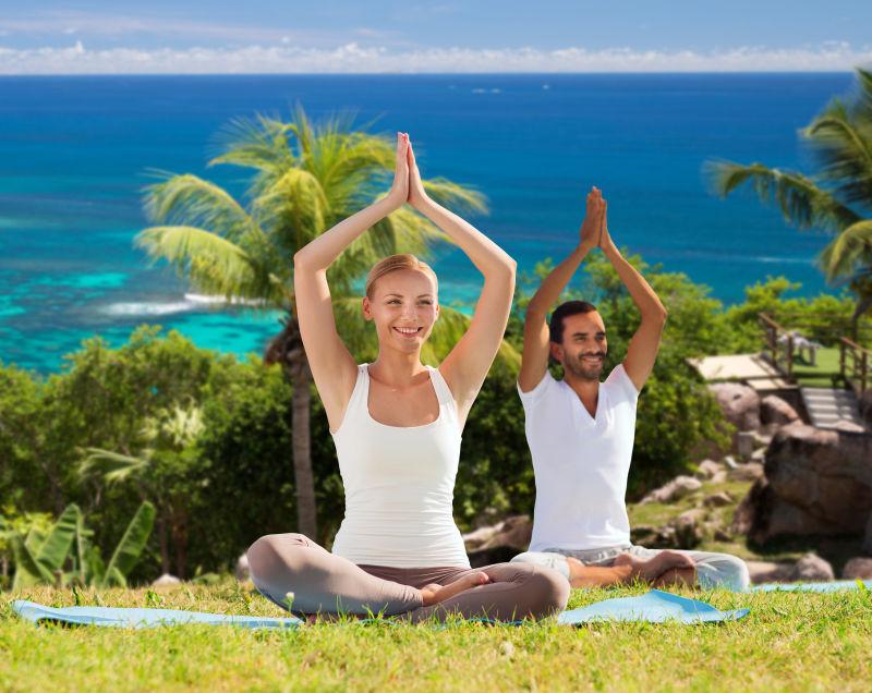 微笑的情侣坐在沙滩上做瑜珈