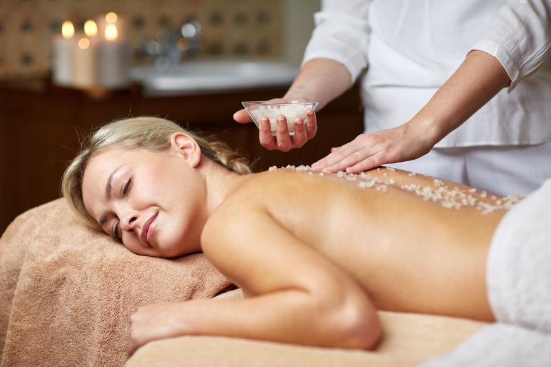 治疗师在温泉浴场拿浴盐为美女按摩