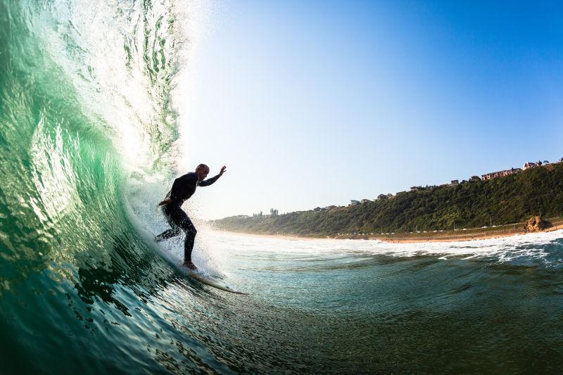 在蓝天下绿色海边上的波涛中冲浪的人