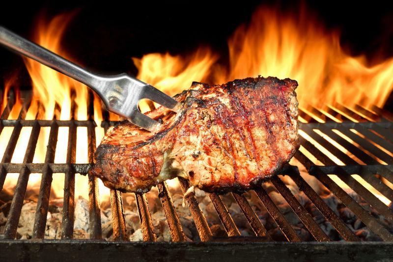 在火焰燃烧的背景下的烧烤架上烤猪排