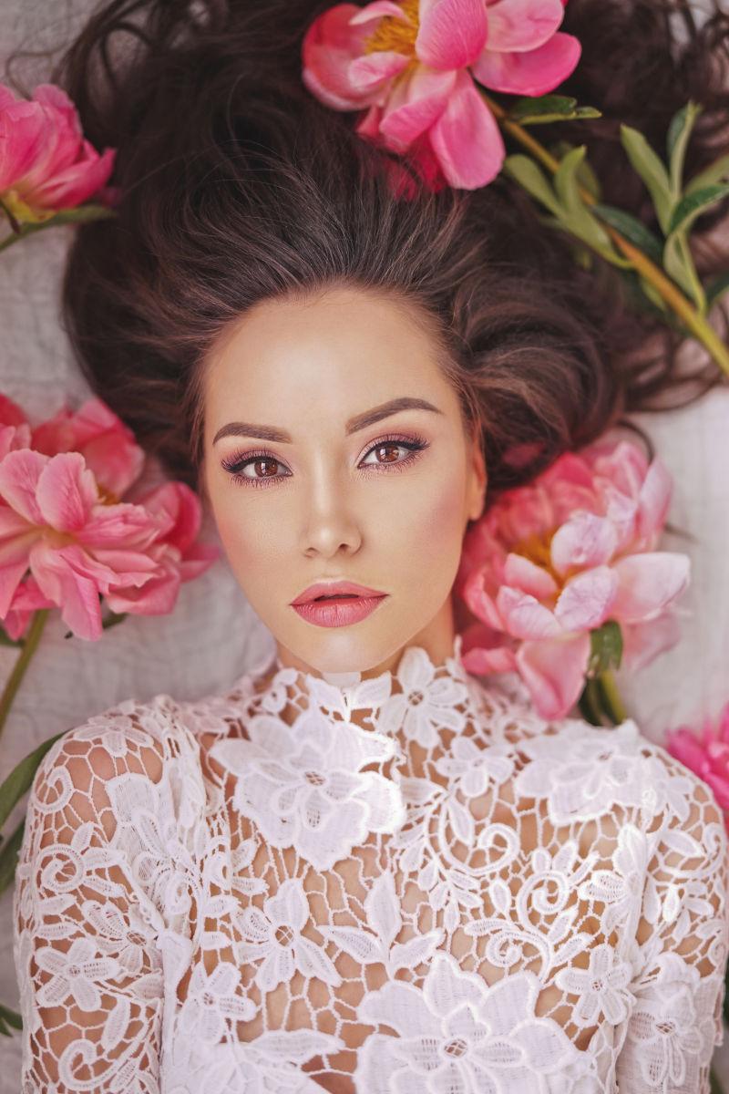 躺在牡丹之间的穿着白色蕾丝衣服的美女