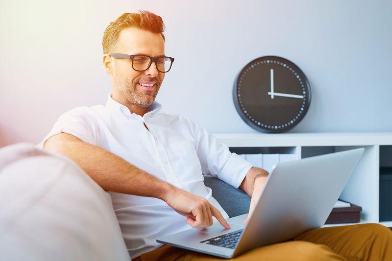 坐在沙发上使用笔记本电脑的快乐男人