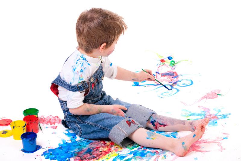 白色背景下的小男孩在用颜料画画